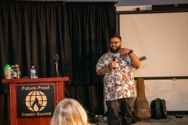 A speaker performing with a guitar at the podium during the Future Proof Creator Summit 2026